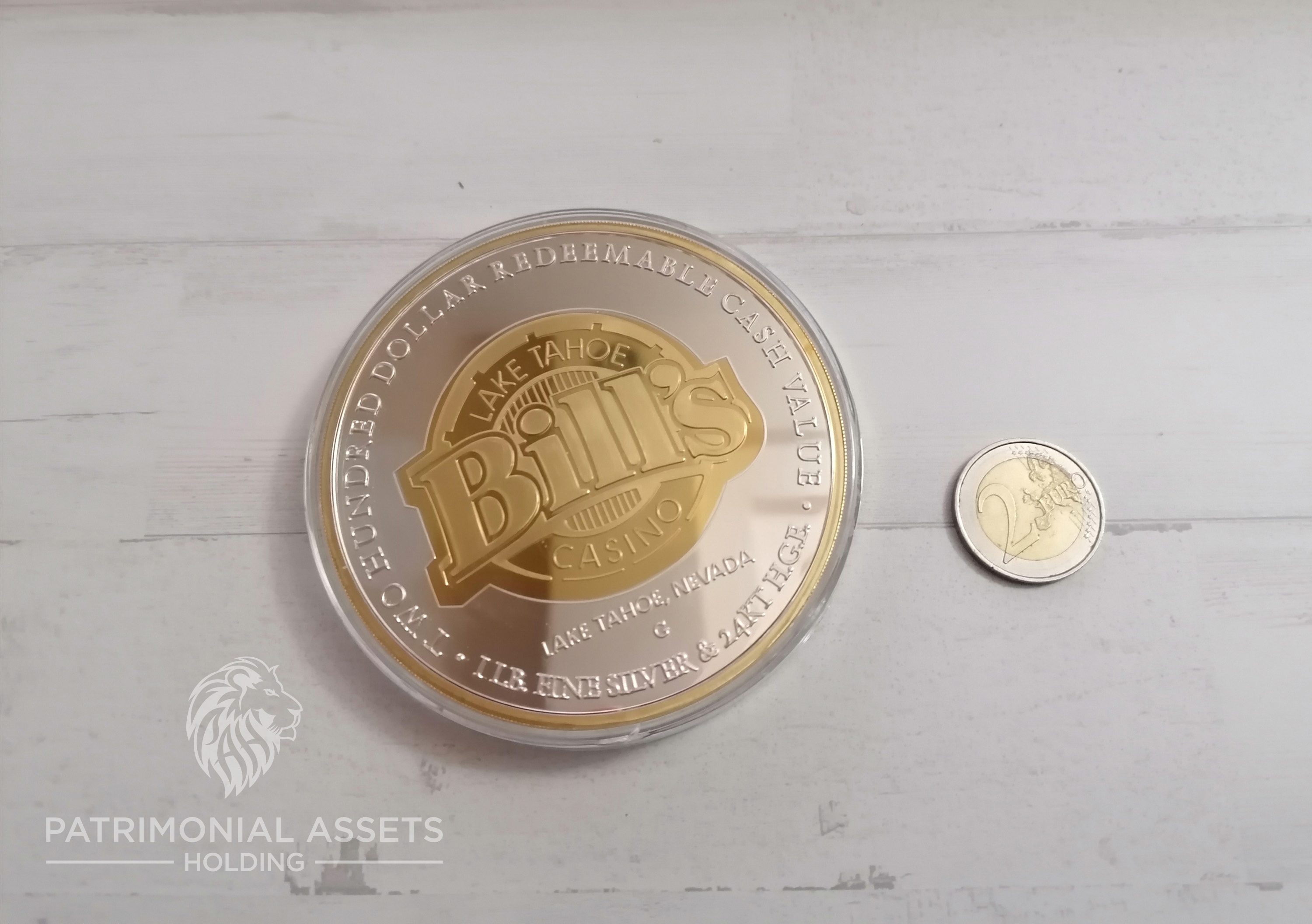 A $200 silver-and-gold casino token placed on a table next to a €2 coin, illustrating its large size.
